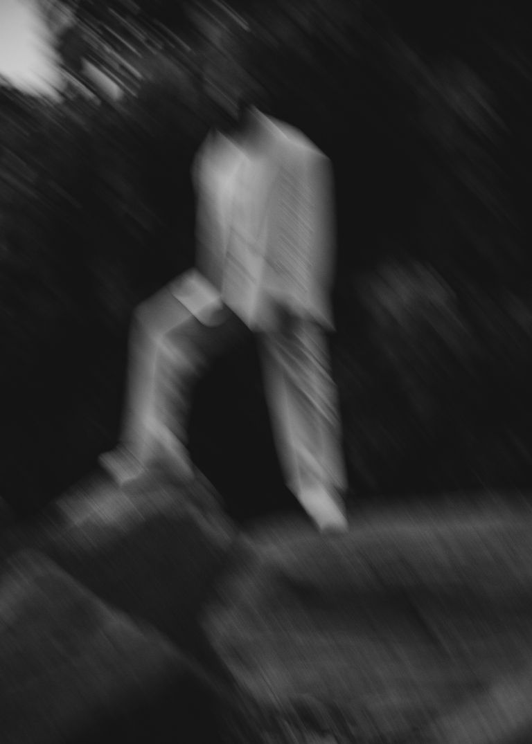 Black and white abstract image of a blurred figure standing on rocks, outdoors.