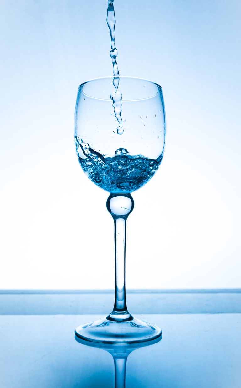 Crystal clear water being poured into a glass with a blue background, capturing motion.