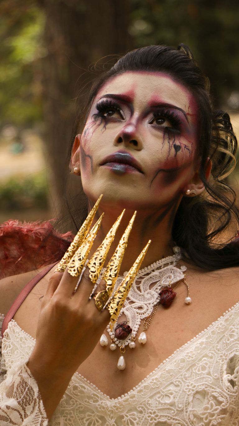 Mysterious woman in gothic cosplay with dramatic makeup and gold claw-like accessories outdoors.