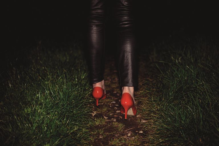 Woman's legs walking outdoors at night in red high heels on grass path.